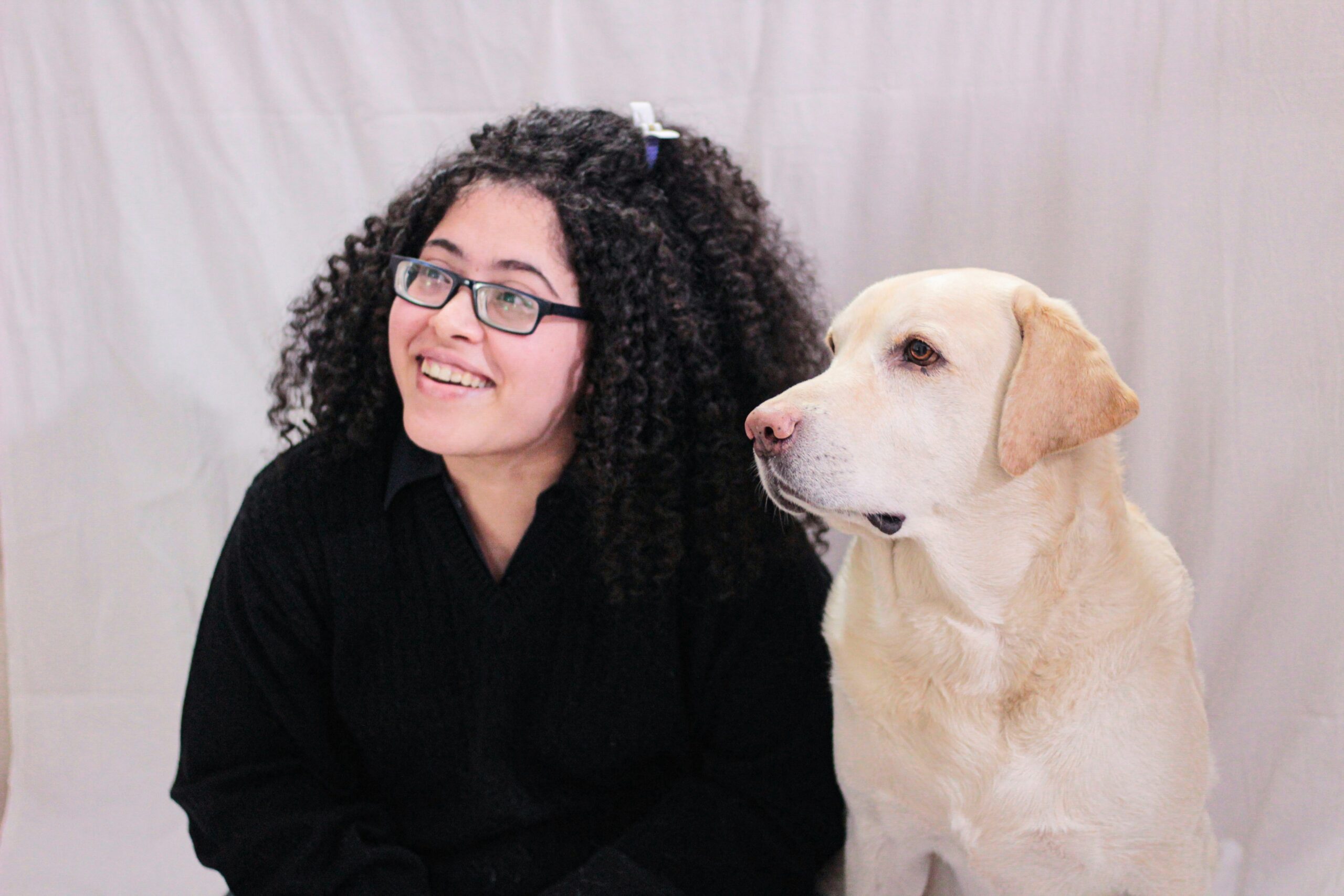 Sarah smiles next to her laptop and a guide dog in training.